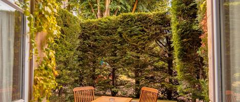 An outdoor patio with a table and chairs, surrounded by greenery and a stone floor.