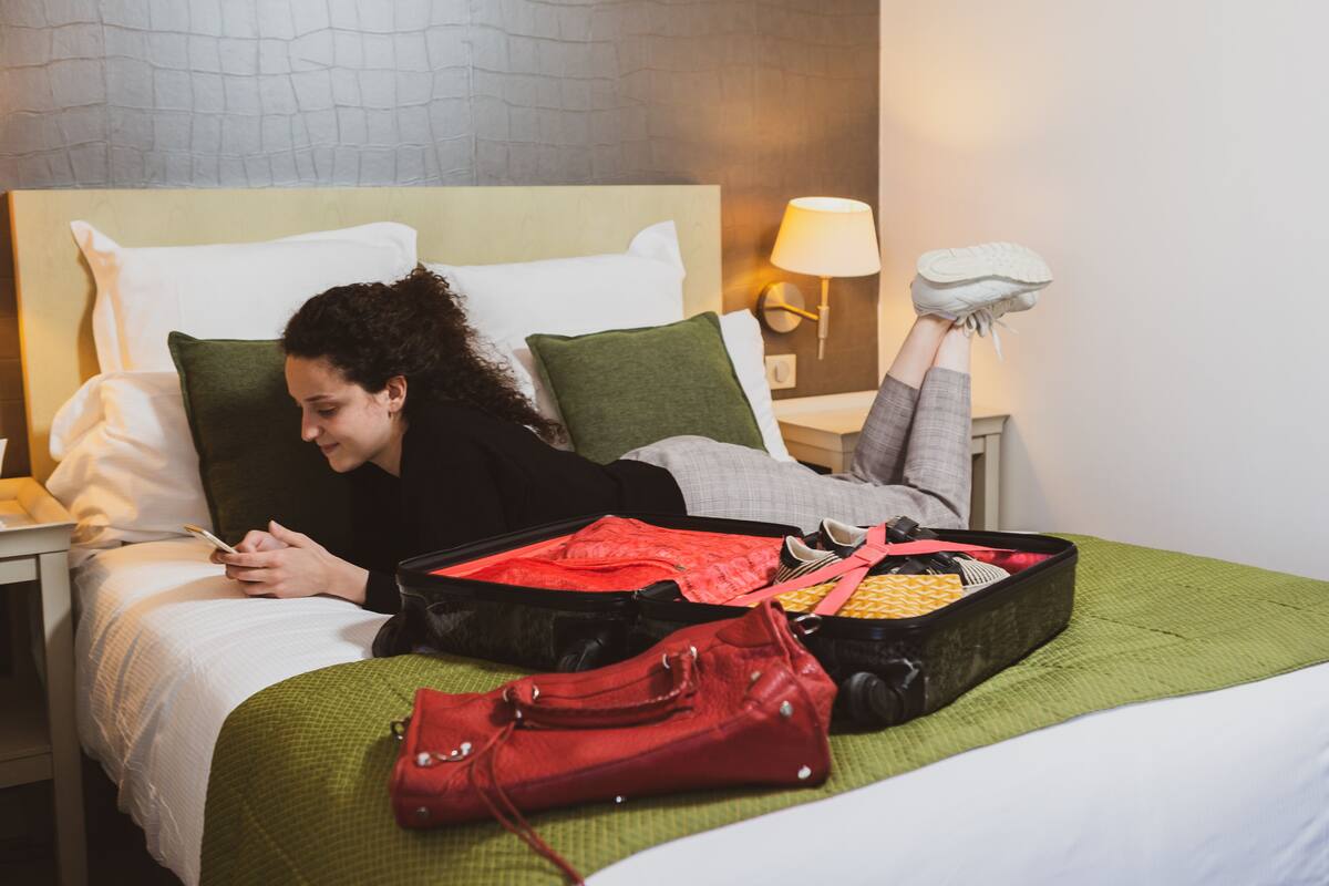 Ein Bett mit Koffer, Handtasche und Schuhpaar daneben.