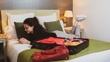 Una cama con una maleta, un bolso de mano y un par de zapatos a un lado.