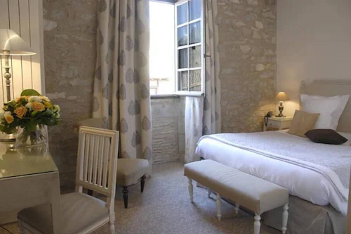 Ein Schlafzimmer mit Steinwand, einem Bett mit weißer Bettwäsche, einem Nachttisch mit Lampe und einem Fenster mit Vorhängen.