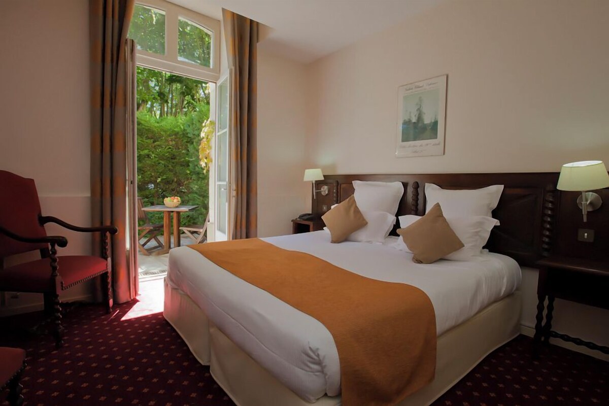 Ein Hotelzimmer mit einem großen Bett, zwei Nachttischen mit Lampen, einem Sessel und einem Fenster mit Vorhängen.