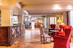 Un hall de hotel con mostrador de recepción, zona de estar y vistas al pasillo.