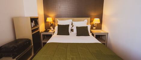 A hotel room with a large bed, two bedside tables, a nightstand, a bench, and a wall-mounted shelf.