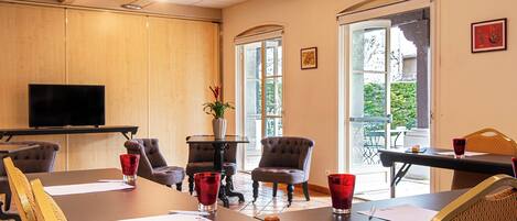 A conference room with a long table, chairs, a television, and a window with a view of greenery.