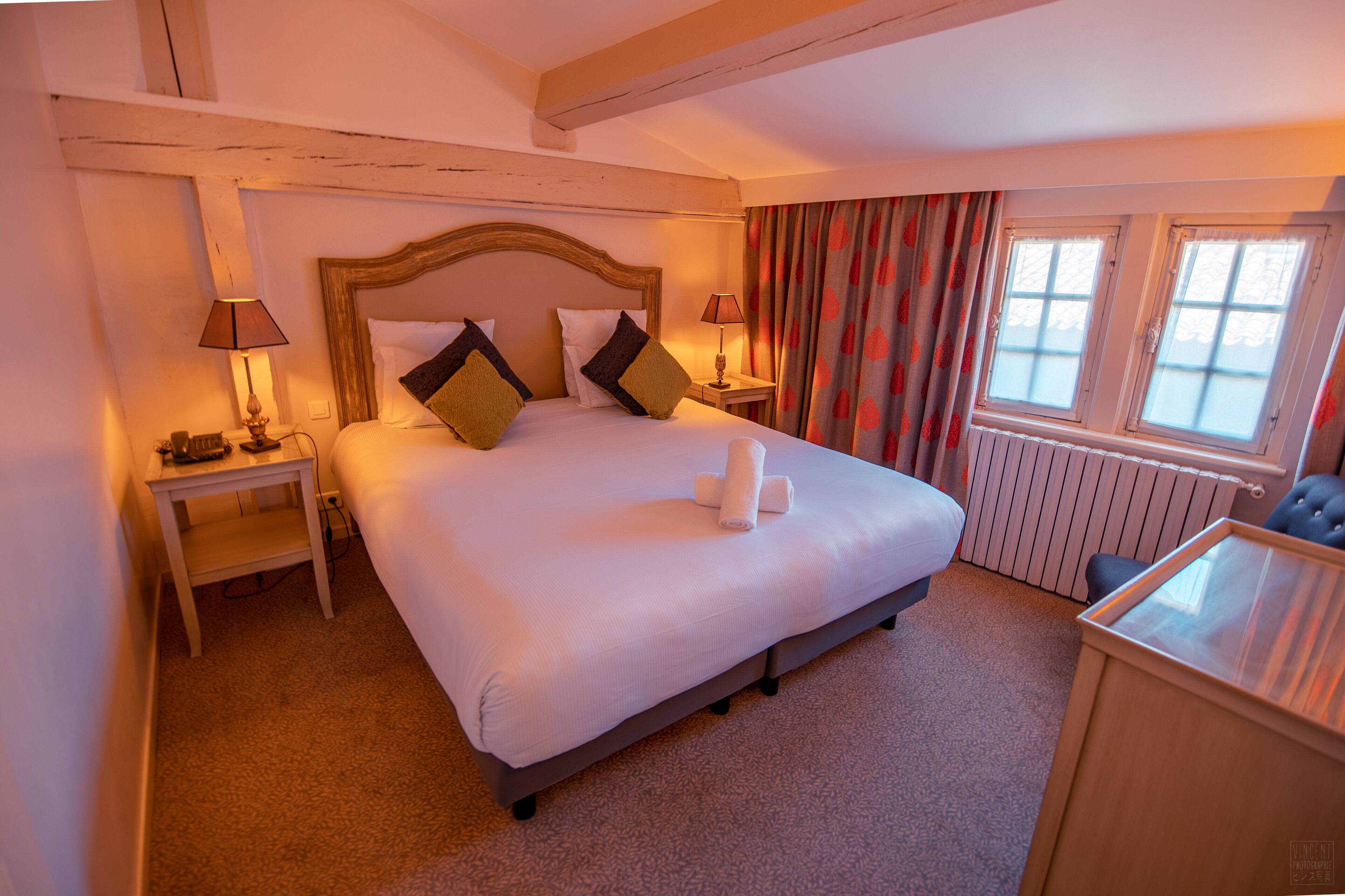 A hotel room with a large bed, two bedside tables, a window with curtains, and a radiator.