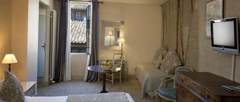 A hotel room with a bed, a desk, a chair, a dresser, a television, and a window with curtains.