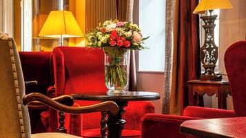 A room with a red upholstered chair, a wooden table with a vase of flowers, and a lamp on a side table.