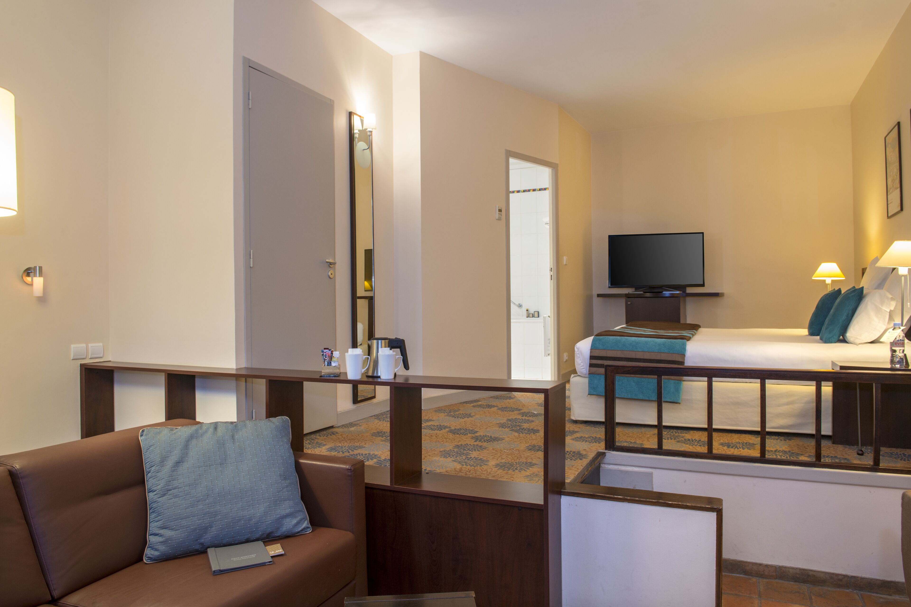 Une chambre d’hôtel équipée d’un canapé, d’un lit, d’une télévision et d’une salle de bain visible à travers une porte ouverte.