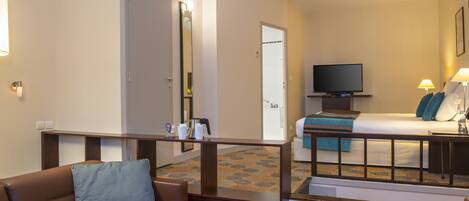 A hotel room with a sofa, a bed, a television, and a bathroom visible through an open door.