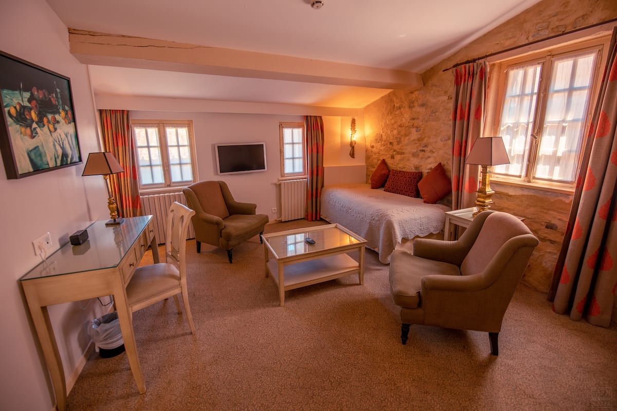 Ein gemütliches Zimmer mit einem Bett, zwei Sesseln, einem Glastisch, einem Schreibtisch und einem Fernseher.