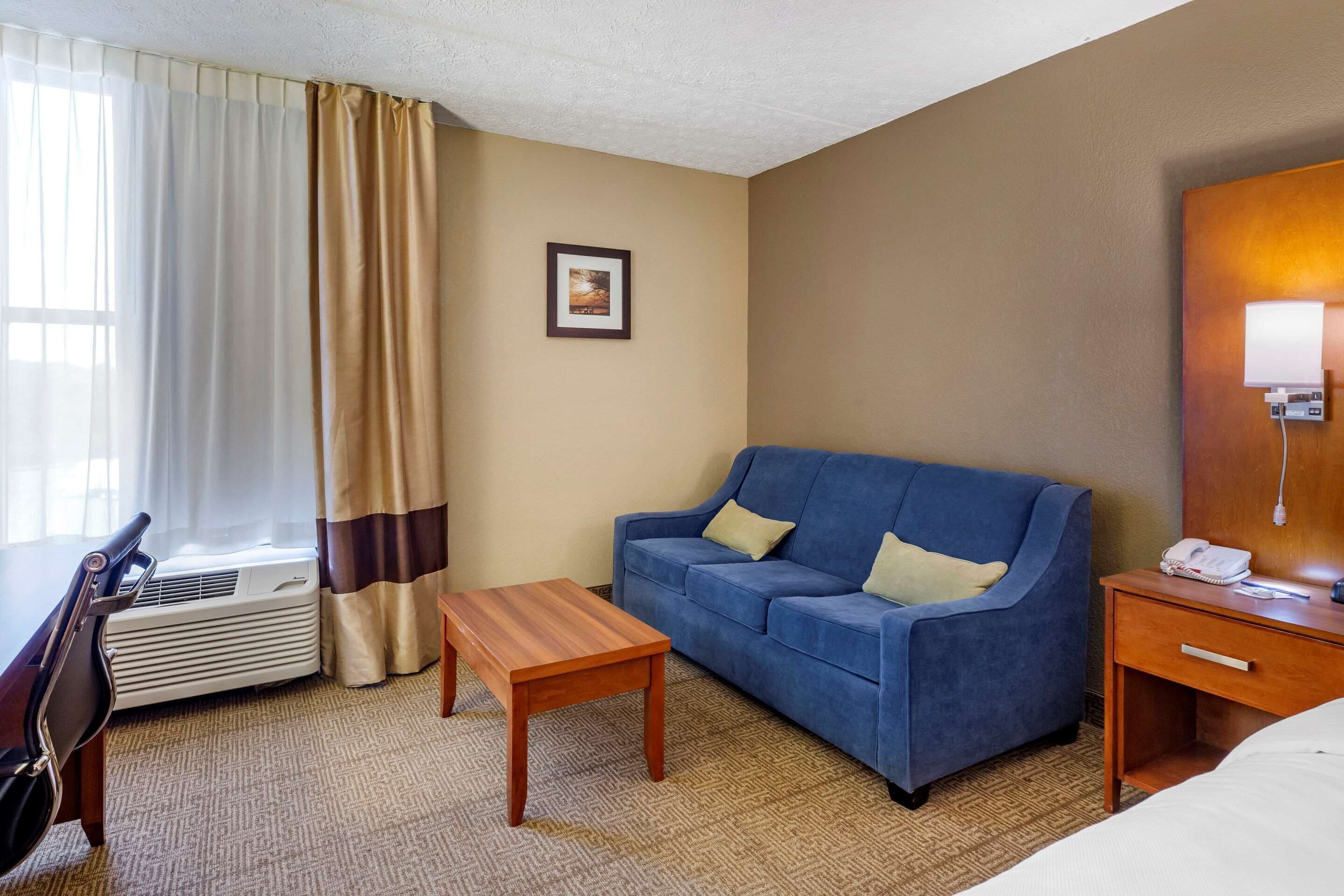 Ett hotellrum med en blå soffa, ett träbord, ett skrivbord med en lampa och en inramad tavla på väggen.