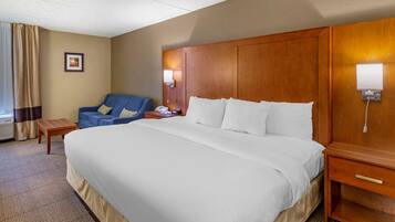 Ein Hotelzimmer mit einem großen Bett, einem Holzkopfende, einem Schreibtisch mit Lampe, einem Stuhl und einem gerahmten Bild an der Wand.