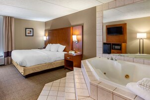 Habitación de hotel con una cama grande, baño independiente con bañera, tocador con espejo y un televisor de pantalla plana sobre el espejo.