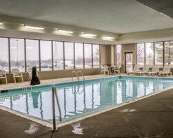 Una piscina interior con agua cristalina, rodeada de ventanas y sillones de descanso.