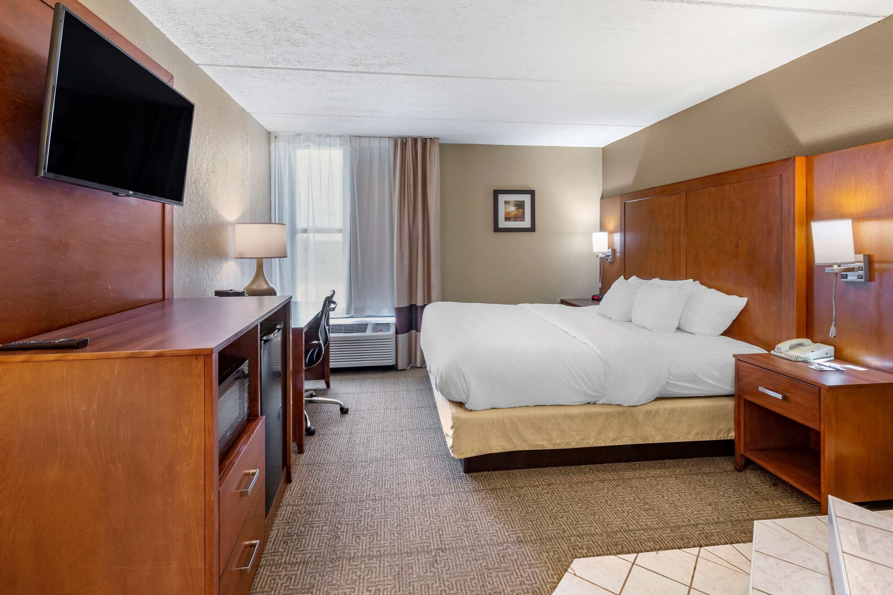 A hotel room with a bed, a desk, a television, and a nightstand.