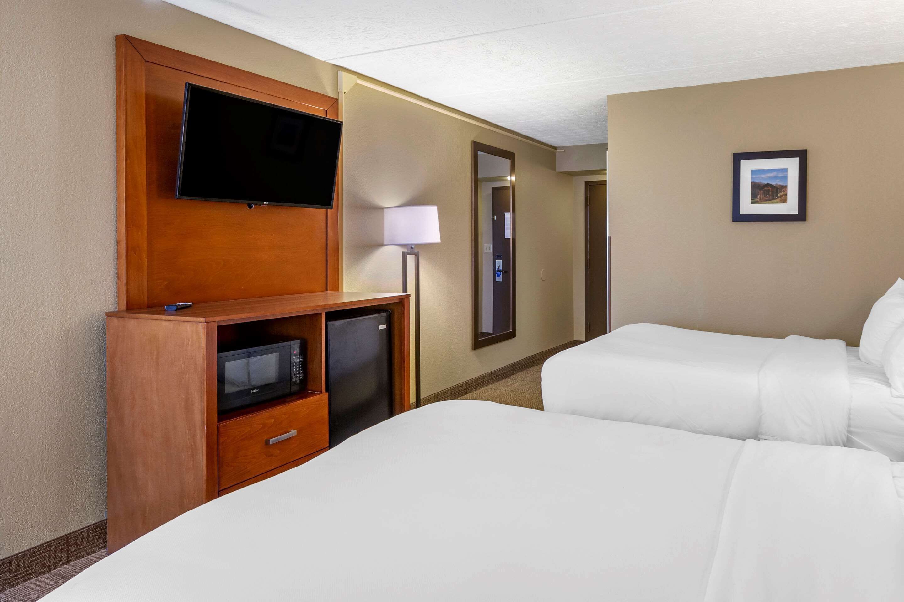 A hotel room with two beds, a TV, a microwave, and a lamp.