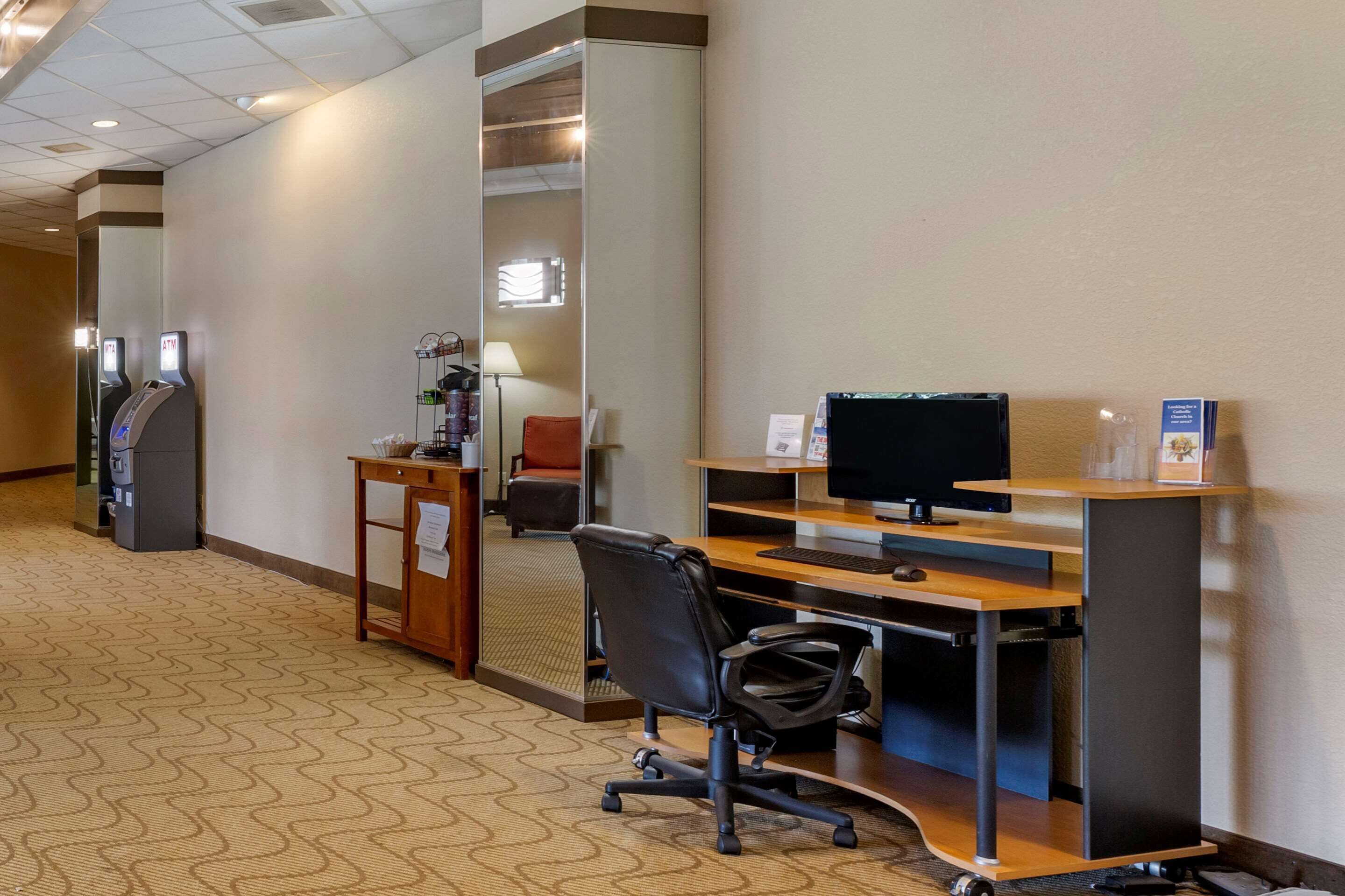 Habitación de hotel con escritorio, silla, ordenador y cajero automático.