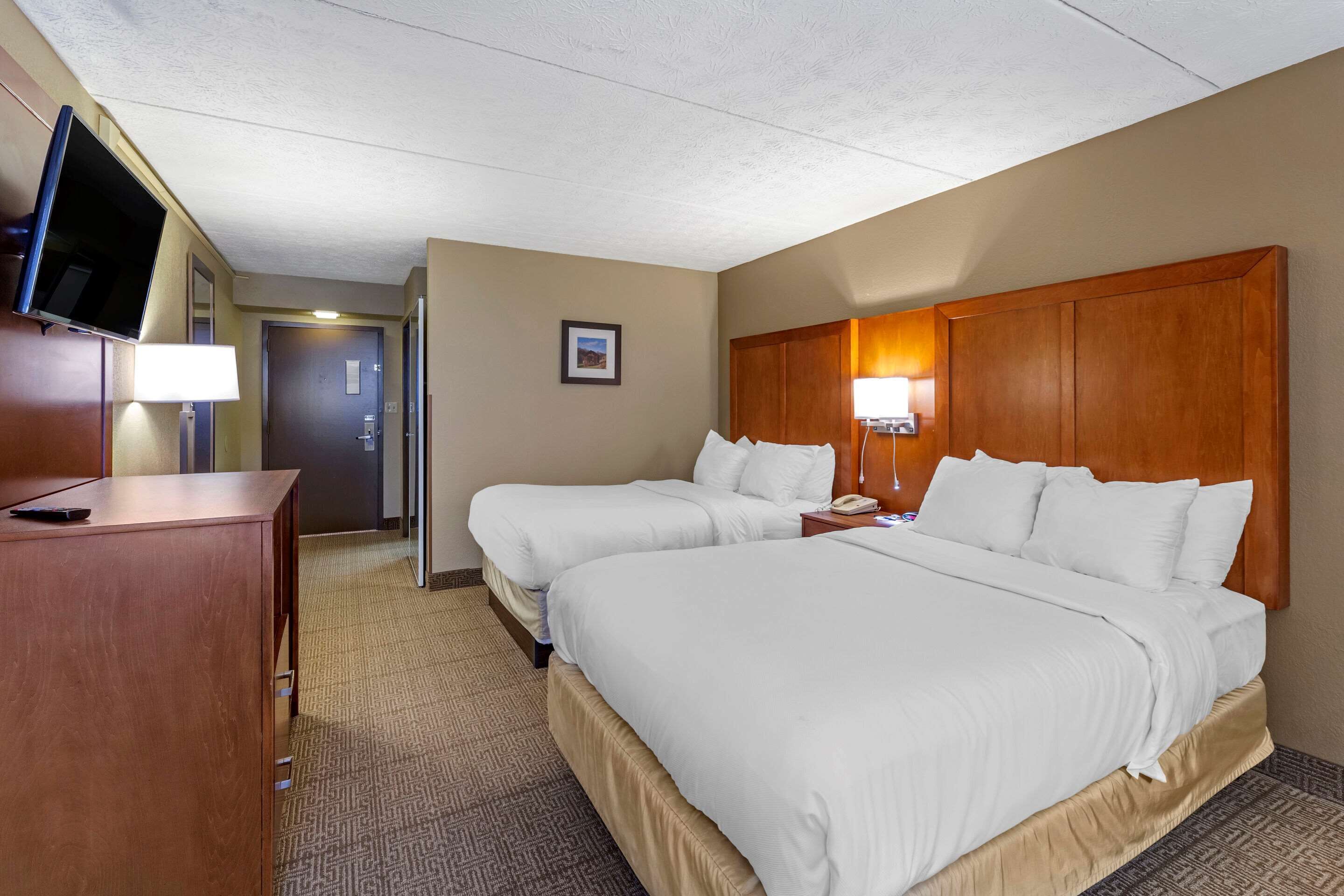 A hotel room with two beds, a TV, a desk, and a lamp.