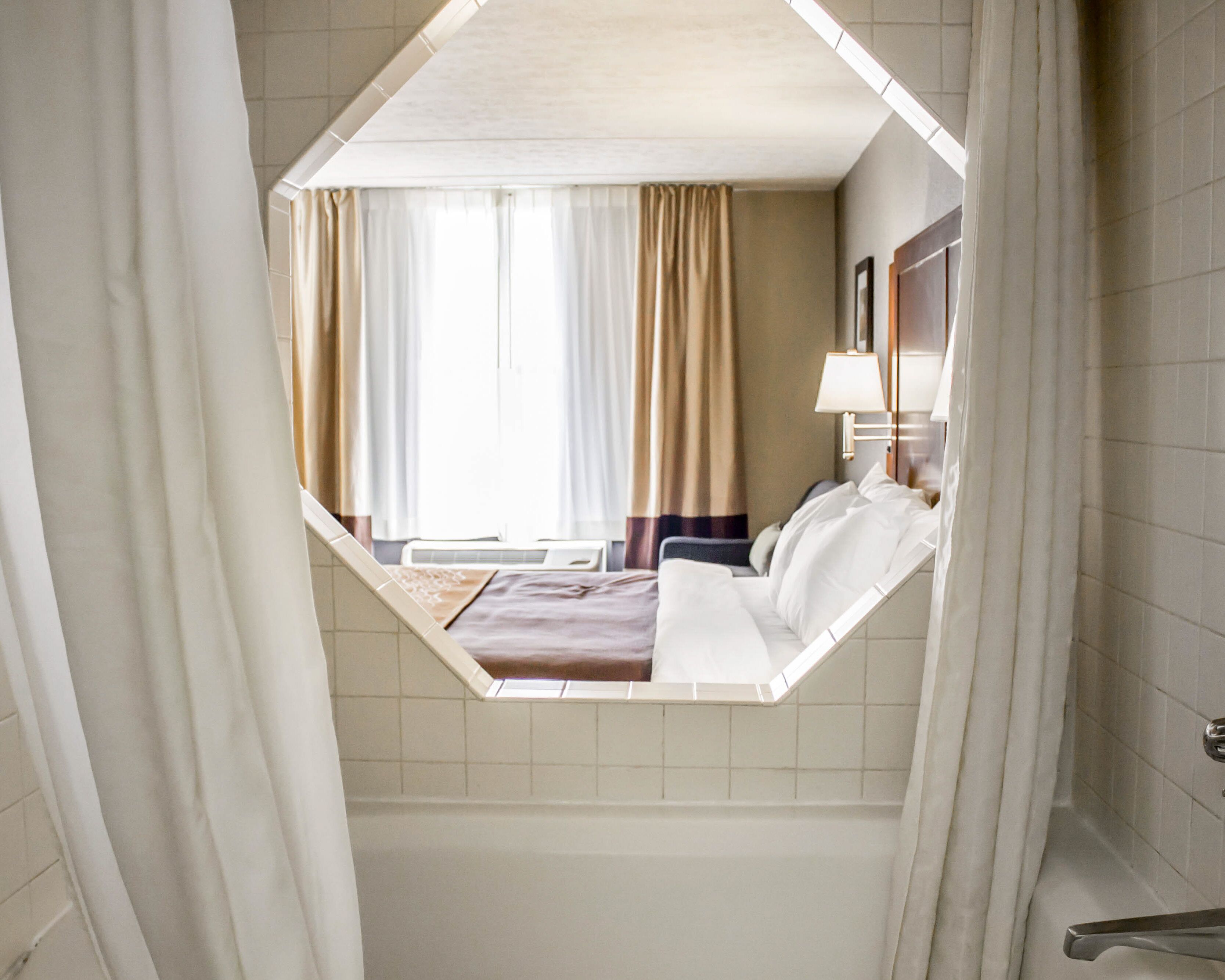 A hotel room with a bed, a window with curtains, a bedside table, and a lamp.