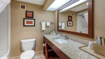 A bathroom with a toilet, sink, and mirror. There are towels hanging on the wall and a framed picture above the sink.