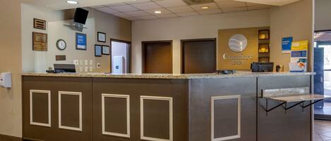 A reception desk with a clock, framed certificates, and a sign for Comfort Inn.