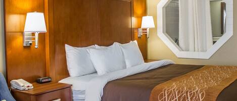 A hotel room with a wooden headboard, two bedside lamps, a large mirror, a bed with white and brown bedding, a blue armchair, and a telephone on the nightstand.