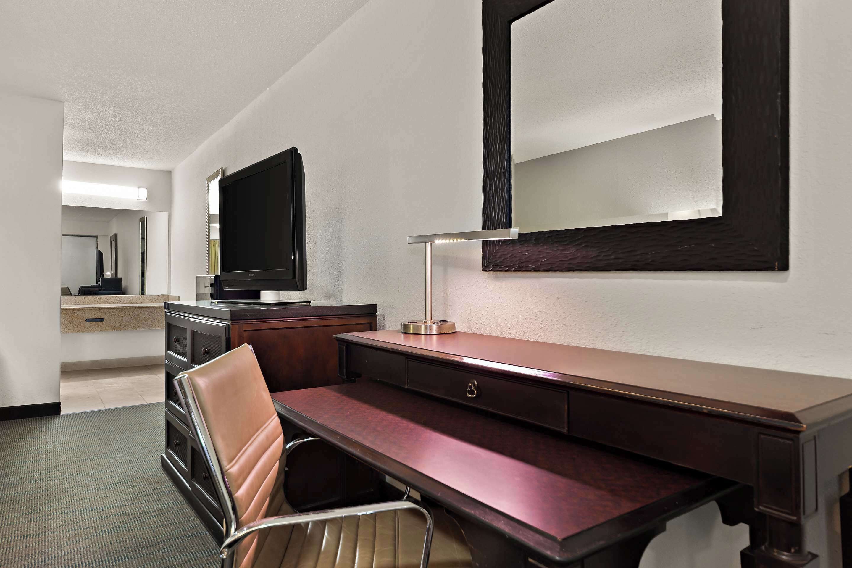 Een hotelkamer met een bureau, stoel, televisie en een grote spiegel.