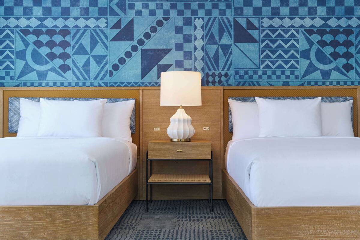Une chambre d’hôtel avec deux lits, une table de chevet avec une lampe et un mur décoré d’un motif.