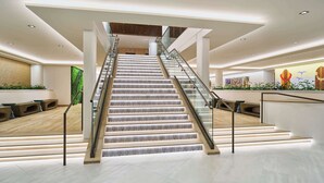 Un hall d’hôtel moderne avec un escalier central, des espaces de détente et un comptoir d’accueil.