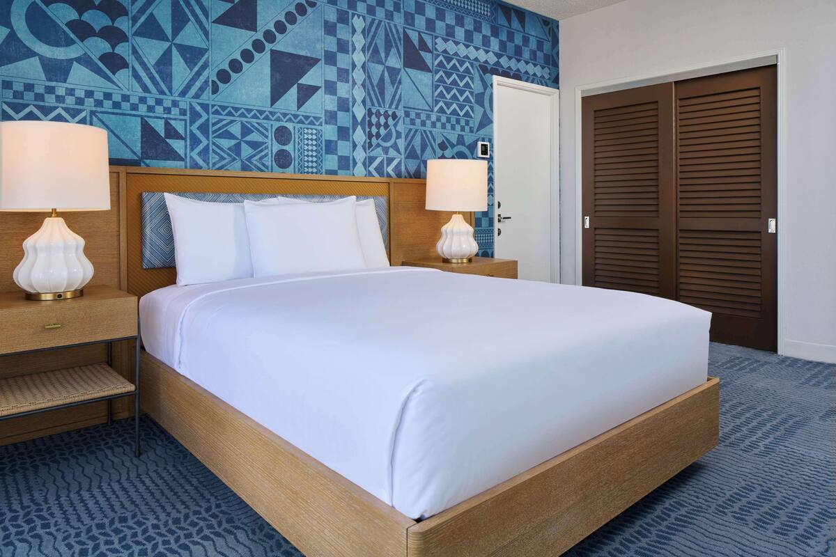 Une chambre d’hôtel avec un lit, deux lampes de chevet, un mur décoré d’un motif et une porte.