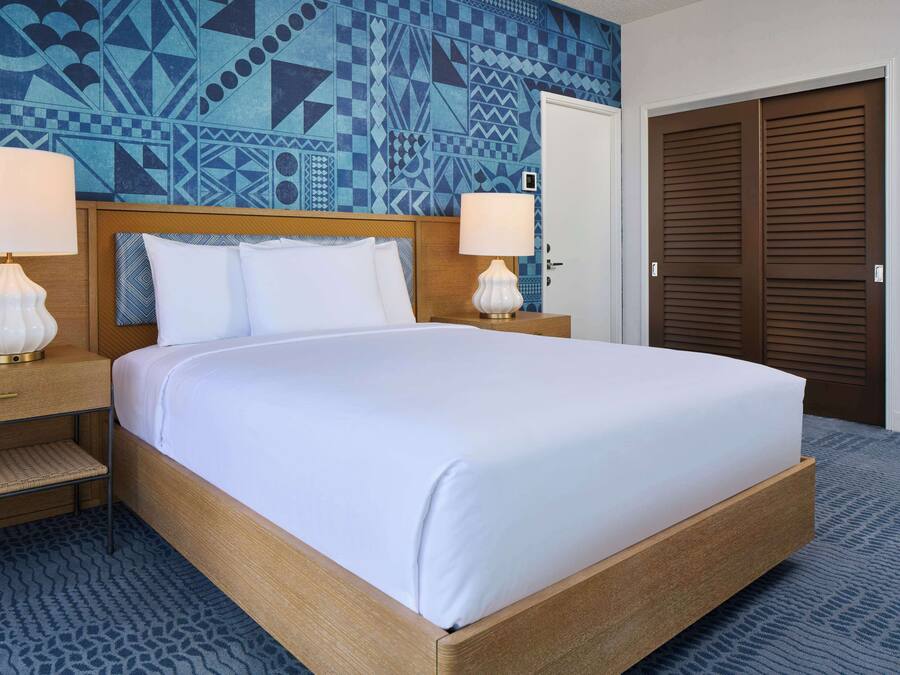 A hotel room with a bed, two bedside lamps, a patterned wall, and a door.