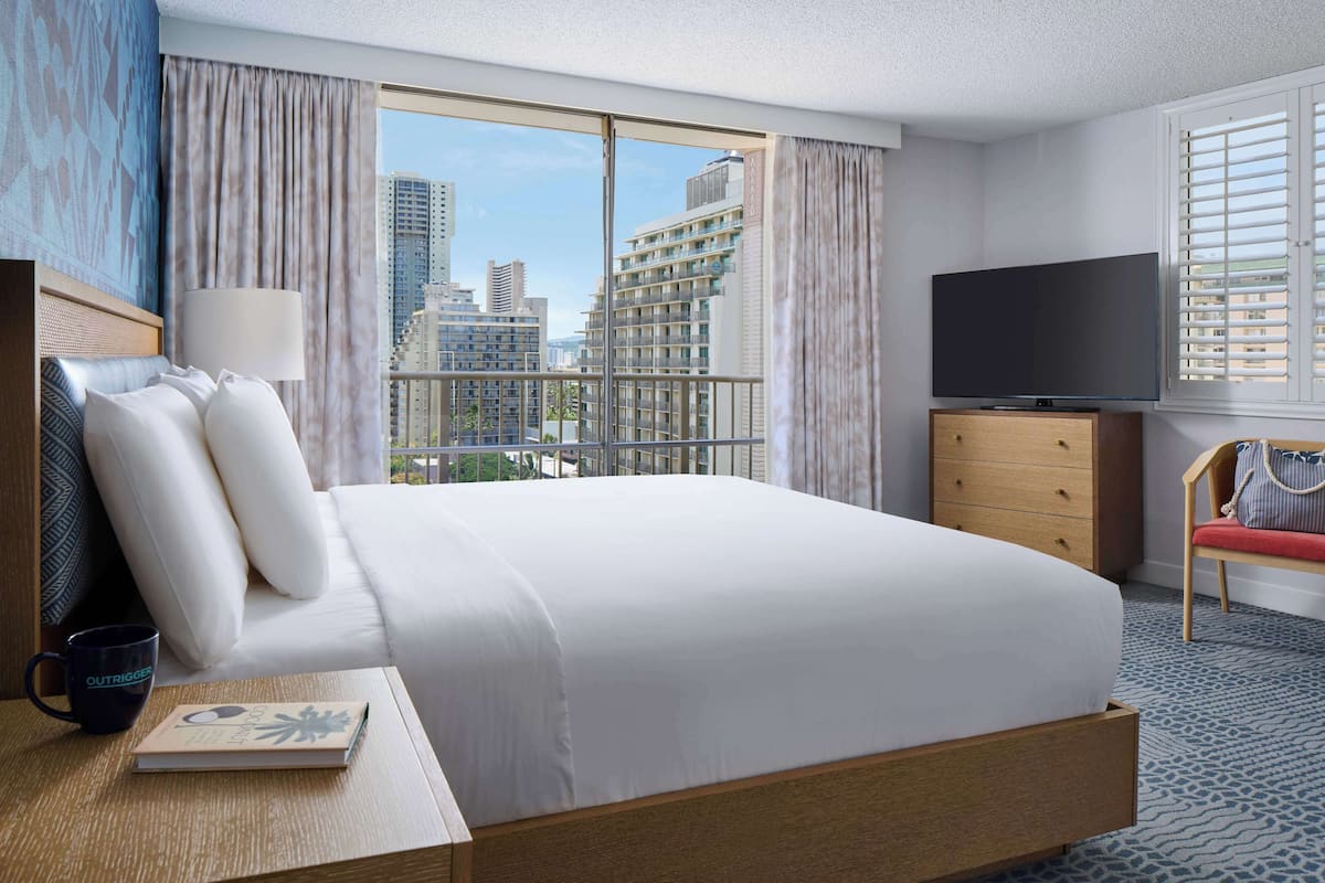 Une chambre d’hôtel avec un grand lit, une télévision, une commode, une chaise et une vue sur les bâtiments de la ville.