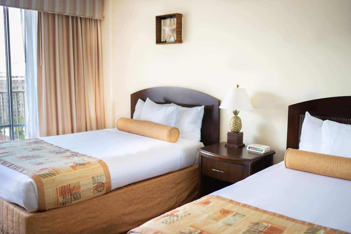 A hotel room with two beds, a nightstand with a lamp, a clock, and a framed picture on the wall.