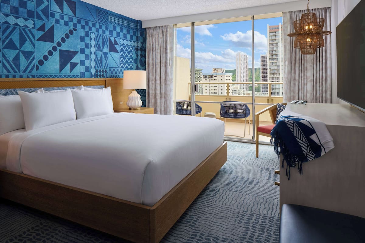 Une chambre d’hôtel avec un grand lit, un bureau avec une chaise, une vue sur la ville et un balcon équipé d’une chaise.