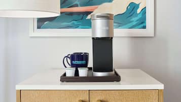A coffee maker, a mug, and a cup on a tray, with a painting in the background.