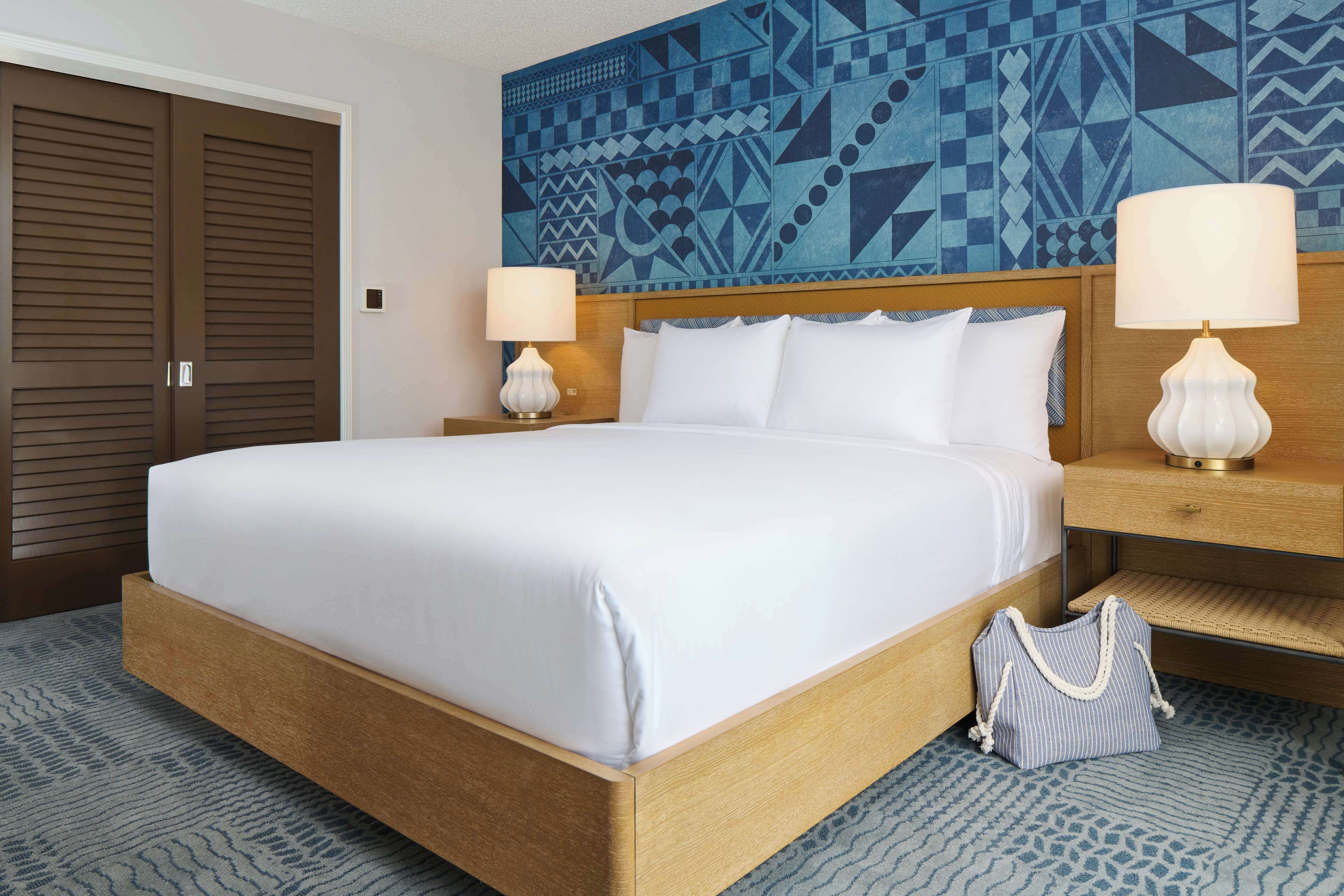 A hotel room with a large bed, two bedside lamps, a patterned wall, and a wooden headboard.