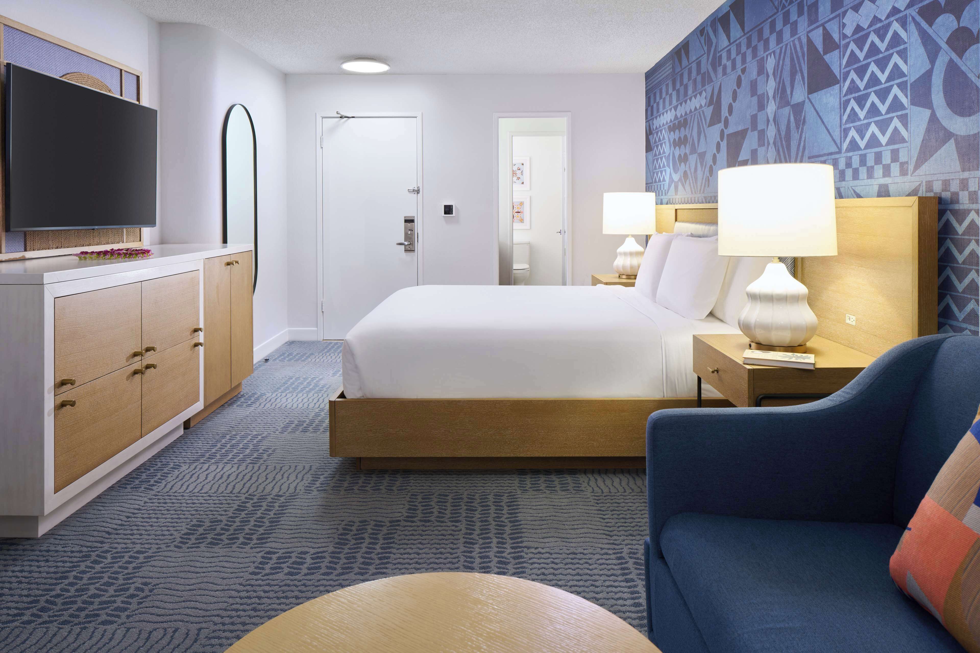 Habitación de hotel con cama, televisión, escritorio con lámpara y pared estampada.