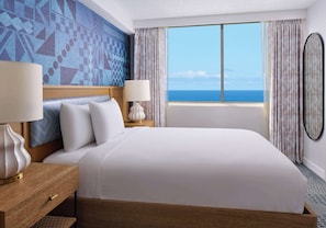 A hotel room with a large bed, two bedside tables with lamps, a view of the ocean, and a patterned wall.