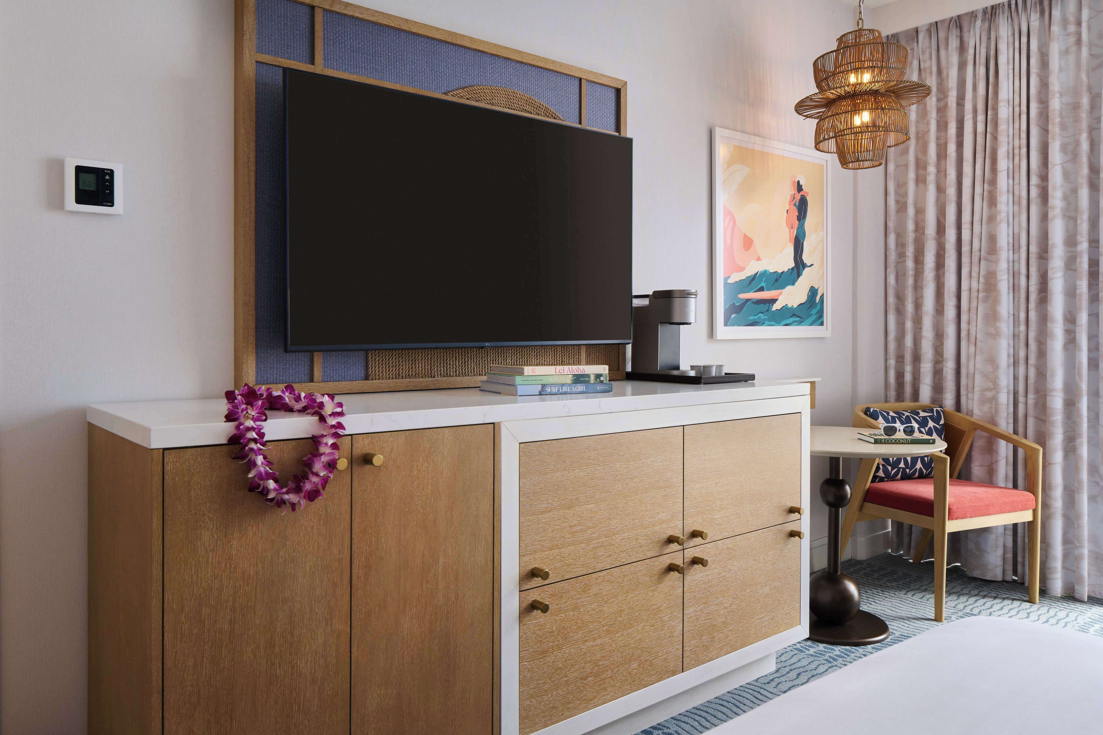 Habitación de hotel con televisor, un aparador de madera, una silla y un adorno en la pared.