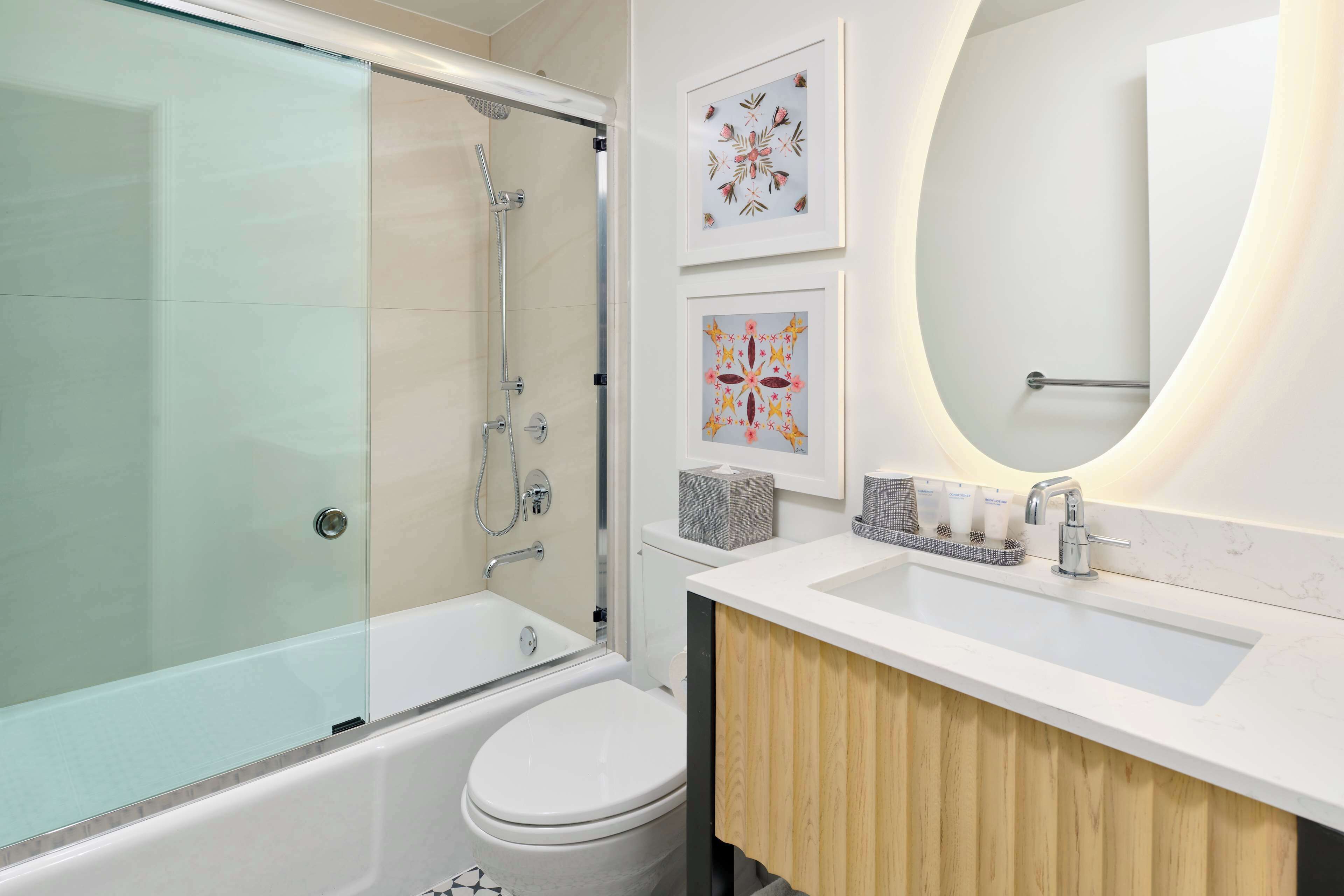 A modern bathroom with a glass shower enclosure, a white bathtub, a toilet, and a vanity with a mirror.