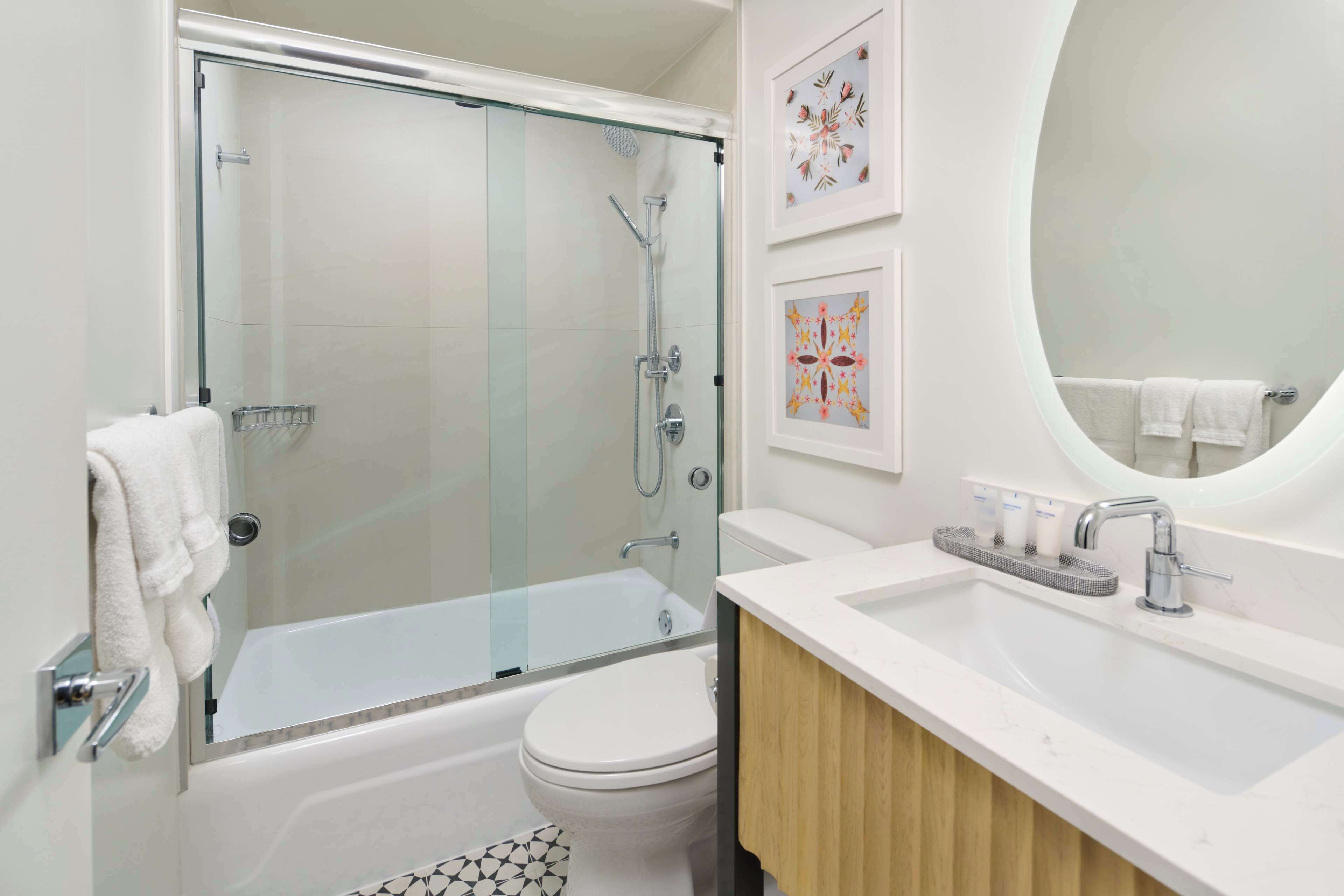 A modern bathroom with a glass-enclosed shower, a white toilet, a sink with a mirror, and decorative wall art.