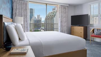 Habitación de hotel con una cama grande, televisión, cómoda de madera, una silla y vista a edificios de la ciudad.
