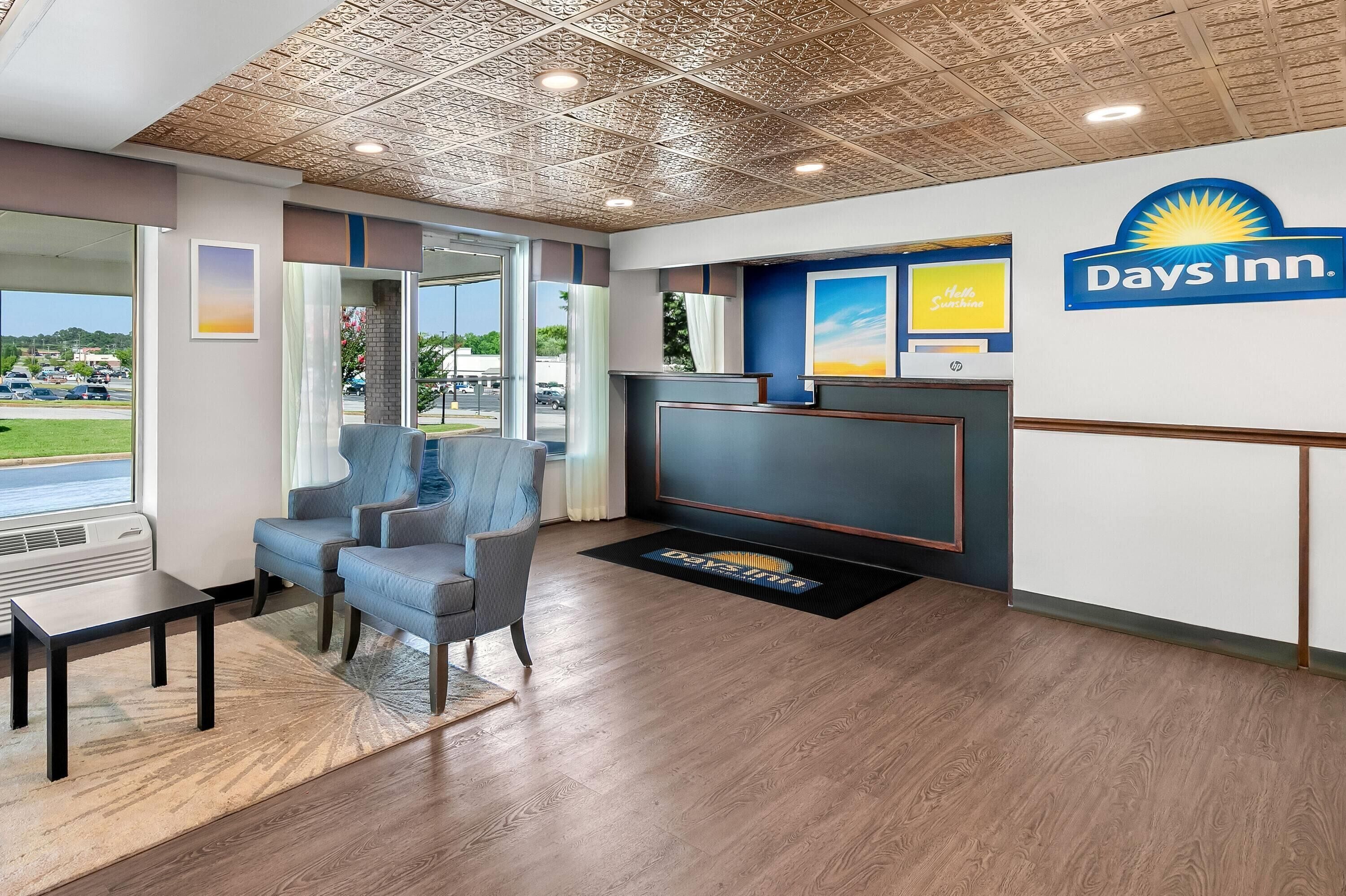 Un área de recepción con una silla azul, un mostrador de recepción y un cartel de Days Inn.