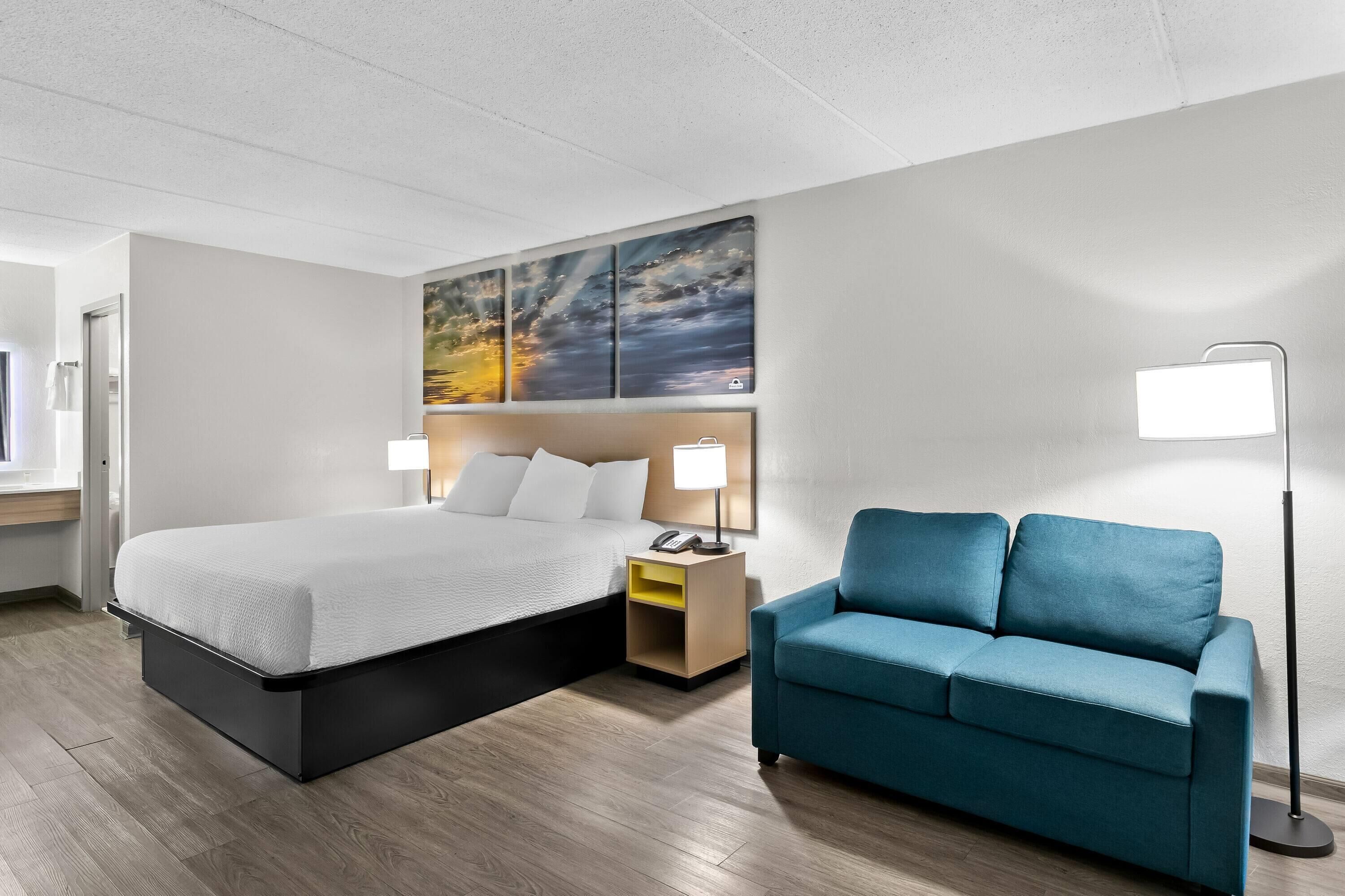 Une chambre d’hôtel moderne avec un grand lit, un canapé bleu, une table de chevet avec une lampe et un tableau au mur.