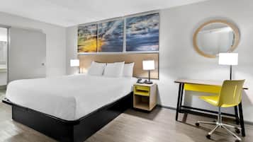 Une chambre d’hôtel moderne avec un grand lit, un bureau avec une chaise, un miroir rond et une table de chevet avec une lampe.