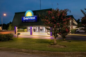 Un hotel Days Inn by Wyndham al atardecer, con techo verde e iluminación morada, y un estacionamiento.
