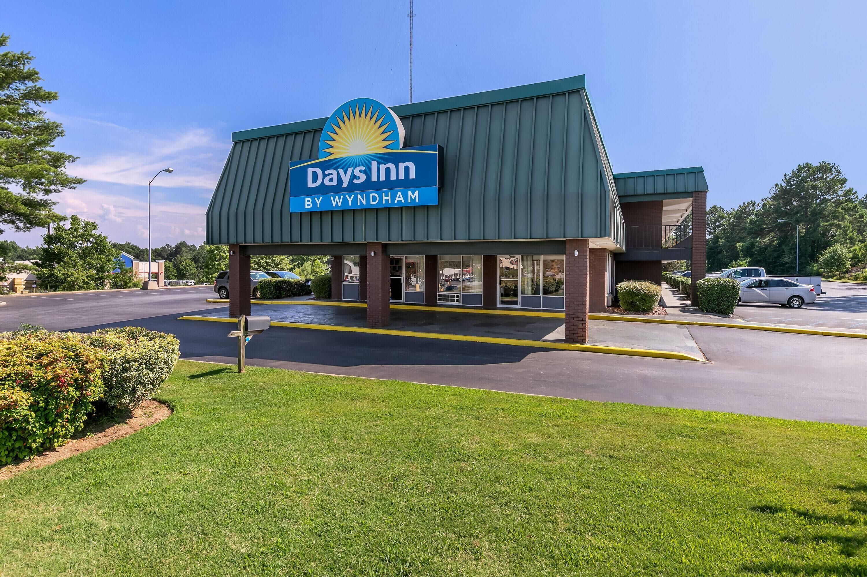 Um hotel Days Inn by Wyndham com telhado verde, estacionamento e céu azul límpido.