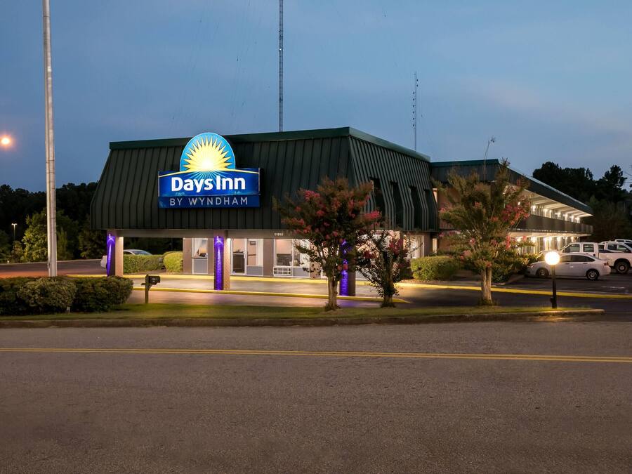 Edificio de Days Inn by Wyndham con techo verde, letrero iluminado y área de estacionamiento.