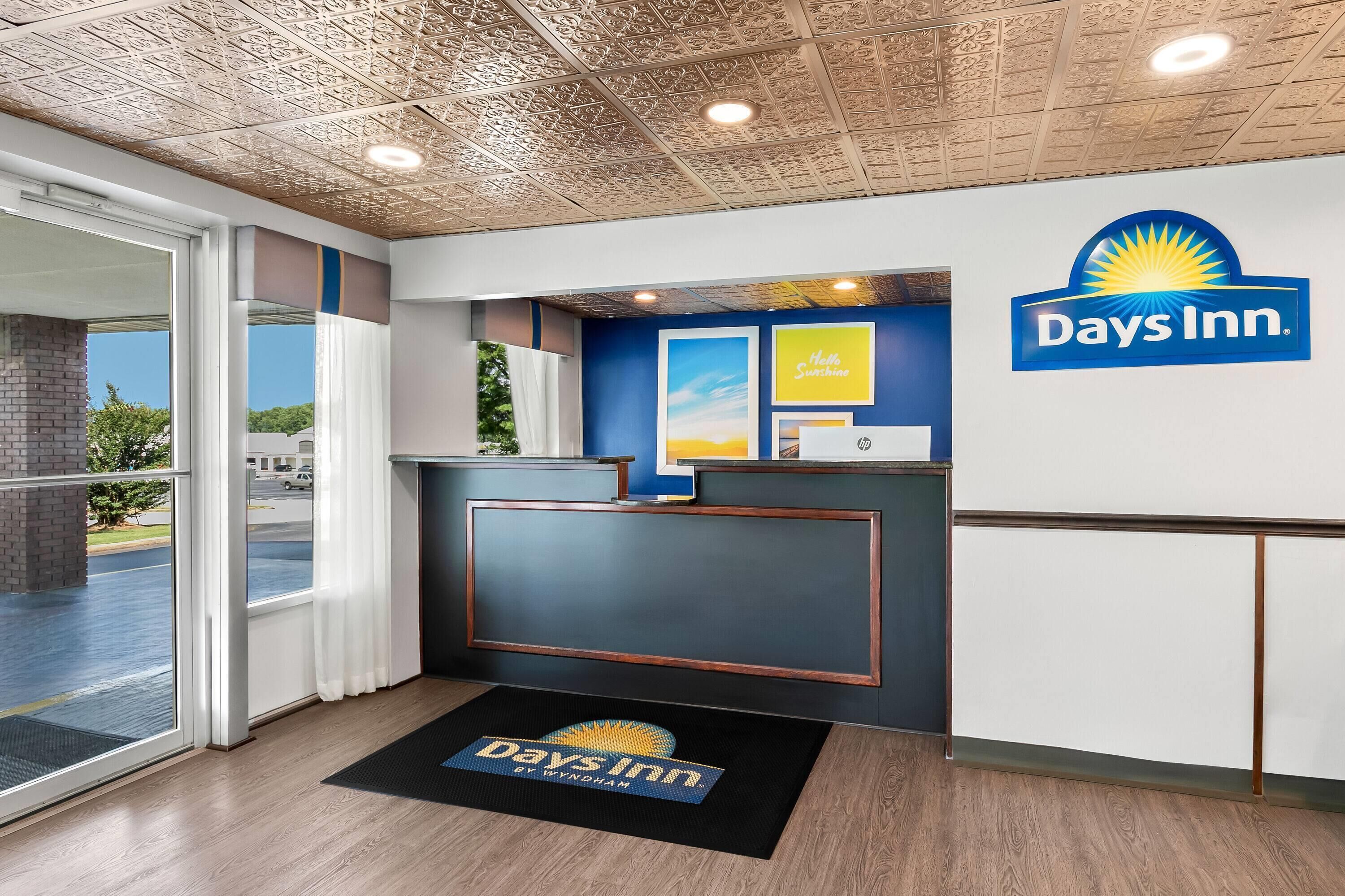 A Days Inn reception area with a modern design, including a reception desk, a large window, and a ceiling with a textured pattern.