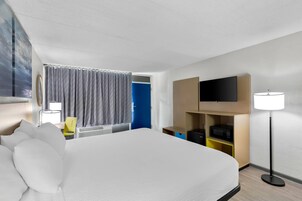 Hotellihuone, jossa on suuri sänky, seinälle asennettu taulutelevisio, työpöytä tuolilla, mikroaaltouuni ja lamppu.